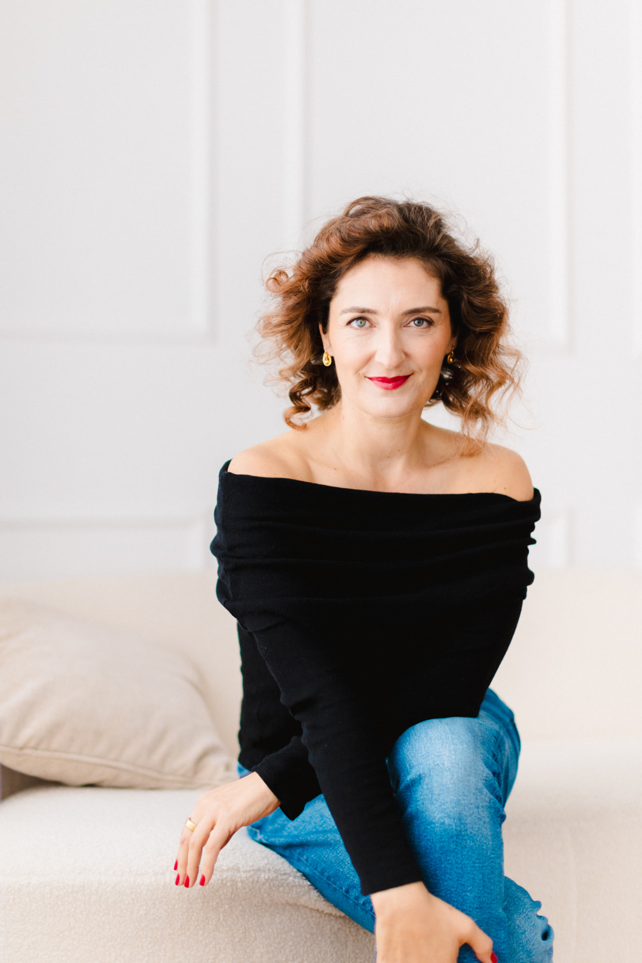 Susana Mota sentada num sofá claro, de blusa preta off-shoulder e jeans